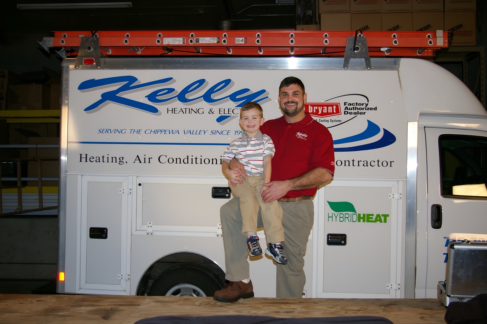 Owner Tim Kelly holding his young son in front of a Kelly Heating & Electric service truck with the Bryant dealer decal