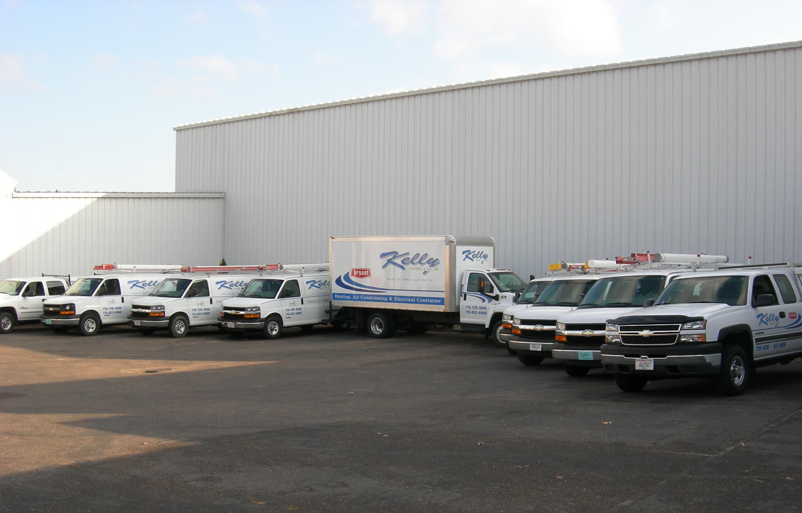 The Kelly Heating & Electric fleet of service vans and trucks lined up outside the warehouse