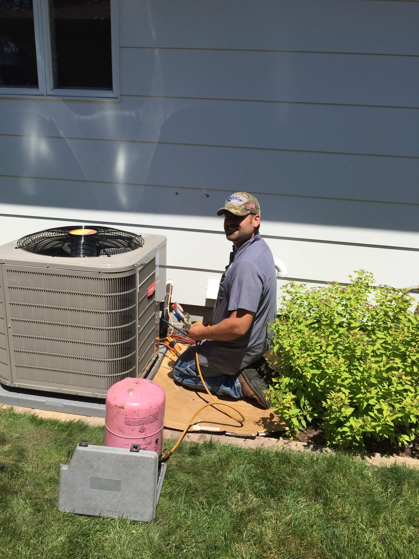 A technician servicing an outdoor air conditioner beside a house