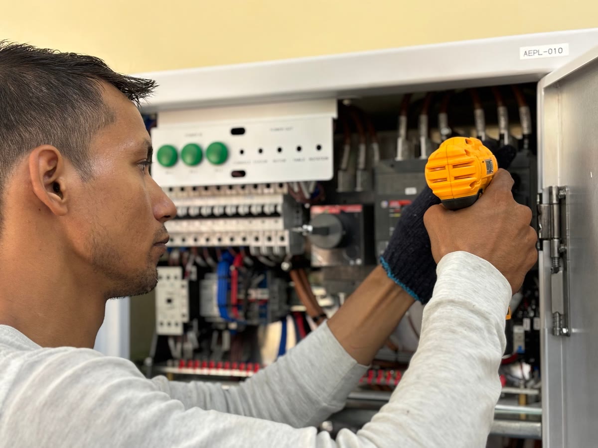 Electrician using a cordless drill at an open electrical panel